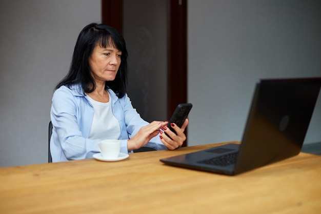 Elderly lady businesswoman relaxing at workplace using mobile phone