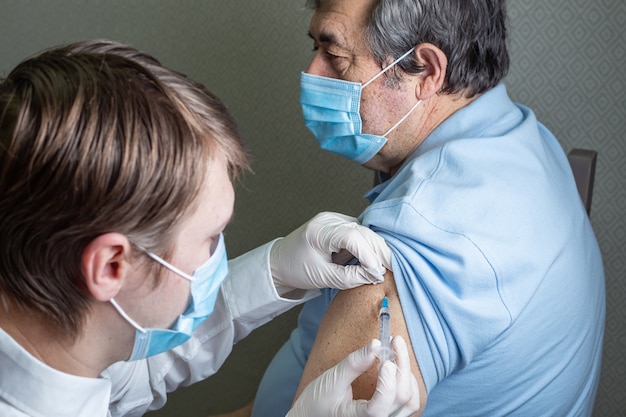 Un uomo anziano di aspetto caucasico con una maschera riceve una dose di vaccinazione contro il coronavirus a casa