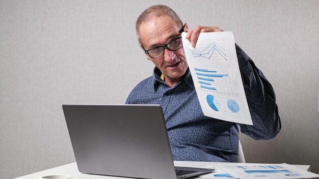 Photo elderly man checks drawings near laptop at white office desk