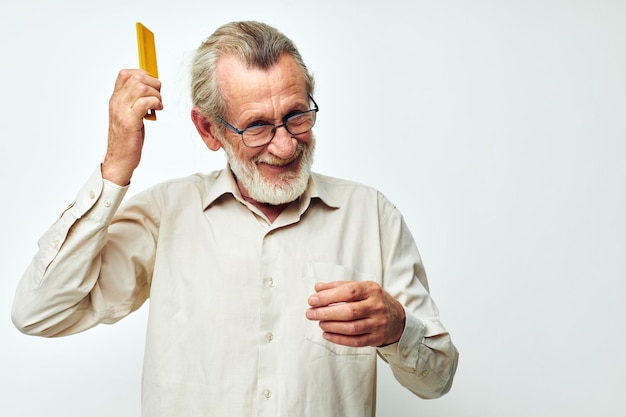 Пожилой мужчина расчесывает волосы желтой расческой в студии на сером фоне
