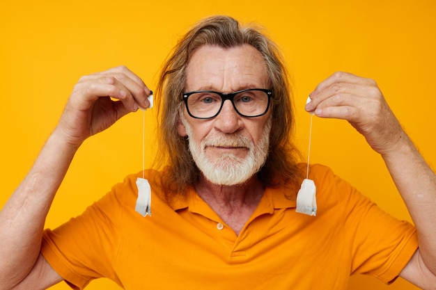 Elderly man disposable tea bags near face yellow background