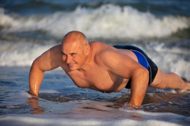 Elderly man doing exercises on the beach A man is pushing up in water Active holiday on the beach