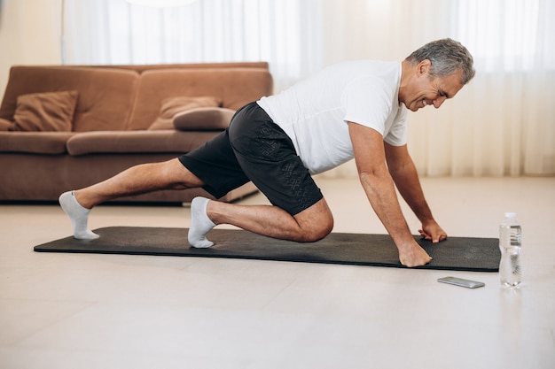 Elderly man doing mountain climber exercises on black yoga mat