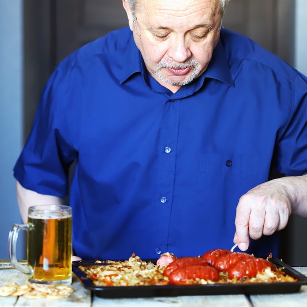 Elderly man eating sausages and drinking beer