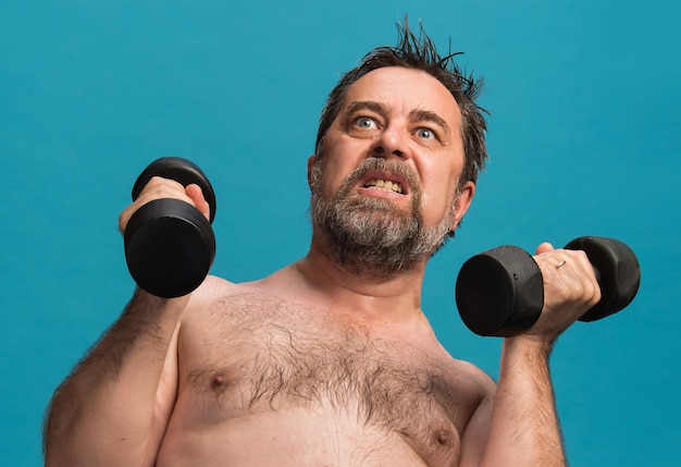 鮮やかな青い背景に強烈なダンベルトレーニングをしている年配の男性