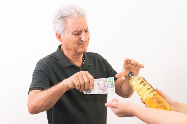 Photo elderly man exchanging 200 brazilian reais bill for a liter of cooking oil