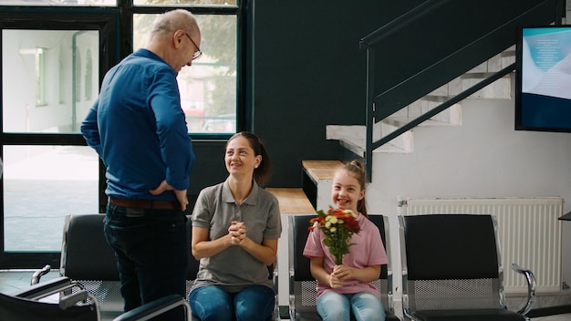 Elderly man feeling healthy after examination, walking after using wheelchair in waiting room lobby. Senior person being cured of physical impairment, talking to woman and small kid.