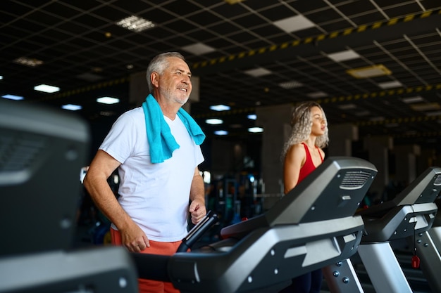 Uomo anziano e trainer femminile sul tapis roulant in palestra