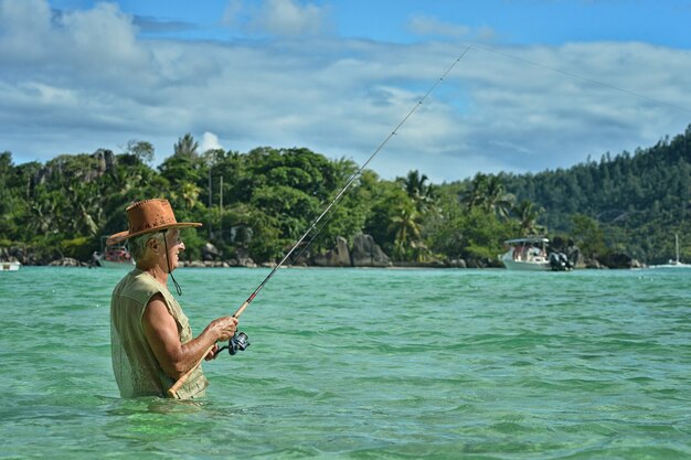 Пожилой мужчина ловит рыбу в море с удочкой