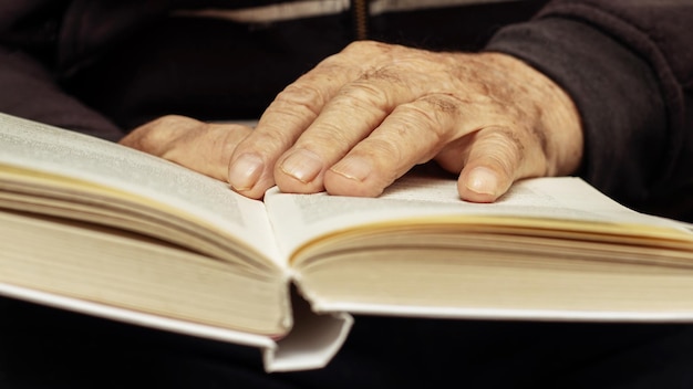 An elderly man a grandfather holds an open book in his hands Leisure for the elderly Reading a book