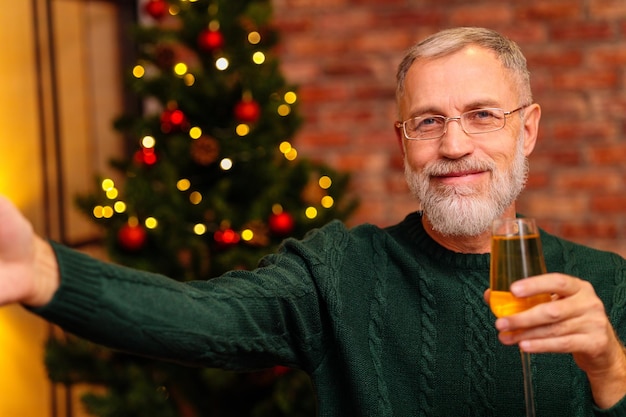An elderly man in a green knitted talking with family by phone video connection near the christmas tree