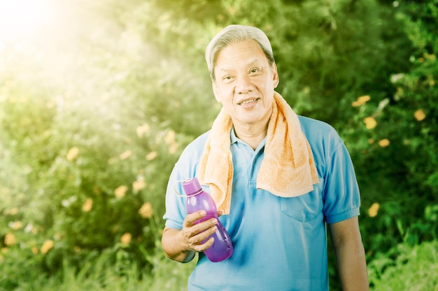 Elderly man holding a bottle of water at park