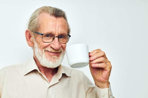 An elderly man holding a mug on a white background and smiling