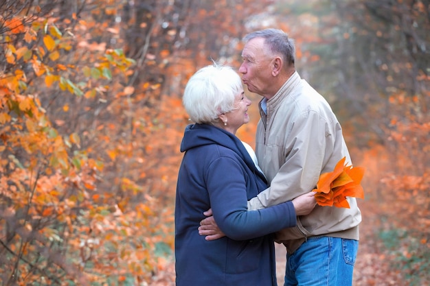 Пожилой мужчина целует женщину в лоб в осеннем парке