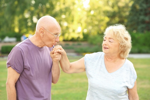 Elderly man kissing hand of senior lady in park