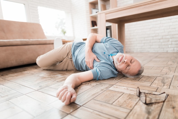 Elderly man lies on floor, clutching heart.