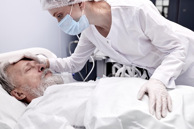 Elderly man lying on bed suffering from disease, female nurse\
checking the temperature