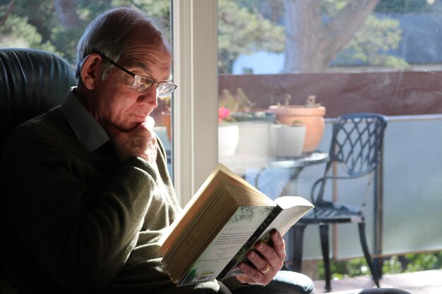 Photo elderly man reading book at home