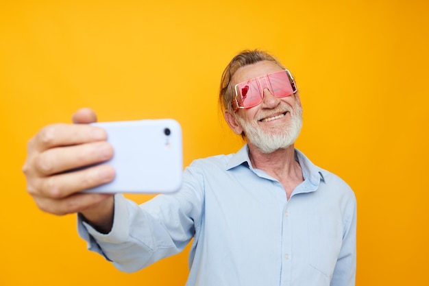 Elderly man in red glasses with telephone yellow background