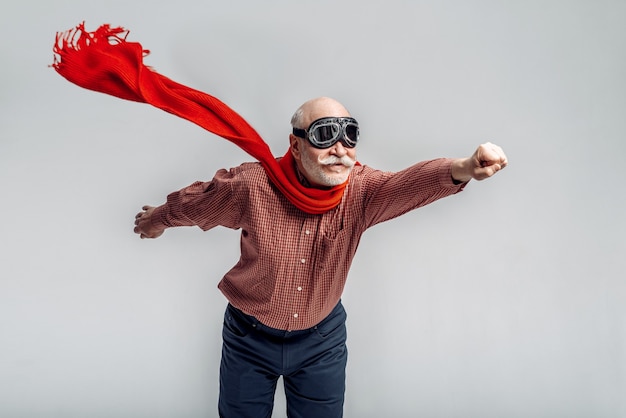 Elderly man in a red scarf and pilot glasses flying like a superman. Cheerful mature senior