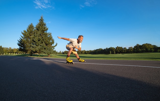 The elderly man rollerblading on the asphalt