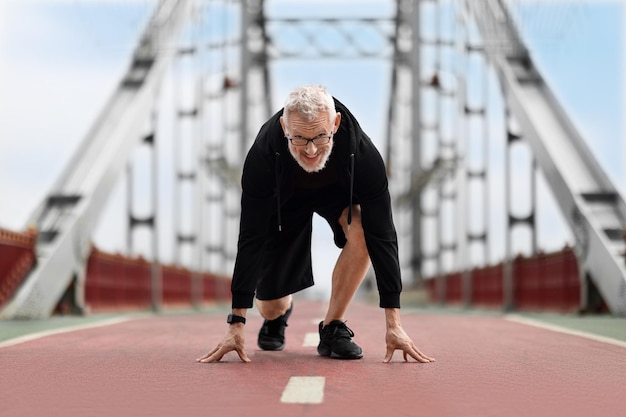 Elderly man runner standing in starting running position outdoor