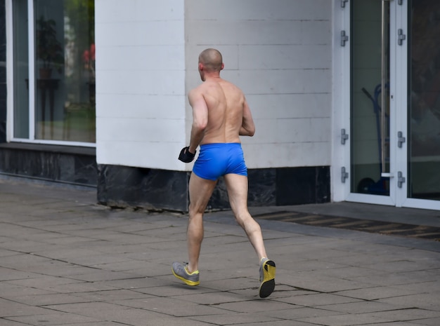 Elderly man in short shorts running cross country in the city in cold weather.