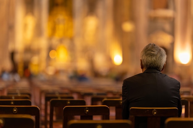 An elderly man sits on a chair in a church