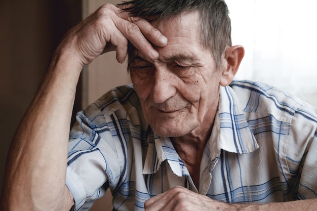 Elderly man sits holding his head, suffering from memory loss