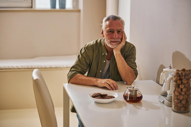 Photo elderly man sitting in his minimalistic kitchen