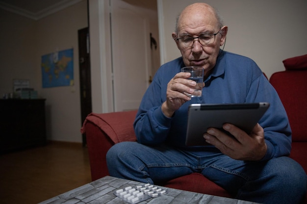 An elderly man takes medicine while talking to his doctor from the tablet