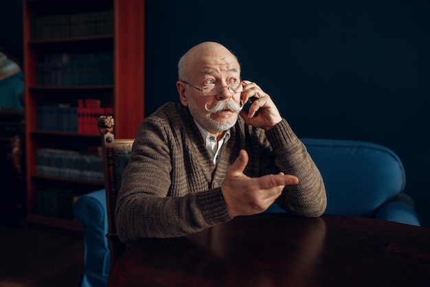 Elderly man talking by mobile phone in home office