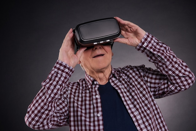 Elderly man in virtual reality glasses on black background.