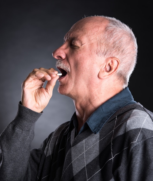 Elderly man wants to take a pill  on a dark background