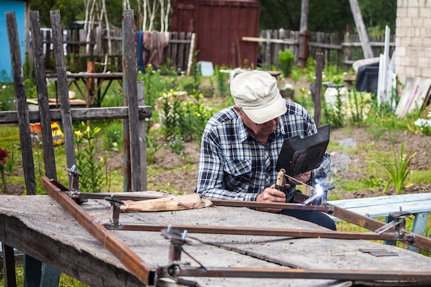 Elderly man welding metal construction at the garden