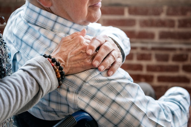 Photo elderly man on a wheelchair holding his wife hand on his shoulder