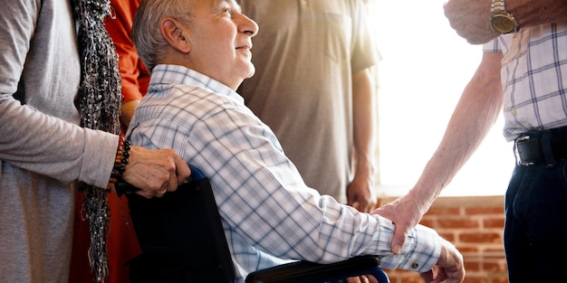 Elderly man in wheelchair surrounded by people showing support and care People show support and care to wheelchair elderly man Caucasian elderly man in wheelchair with friend supports