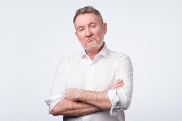 Elderly man in white shirt with his arms crossed looking depressed and annoyed