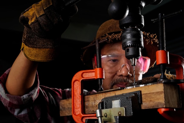 An elderly man with a blacksmith\'s beard is using a platform\
and a drill to drill holes in a smithy