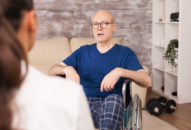 Elderly man with disabilities consulted at home by nurse.