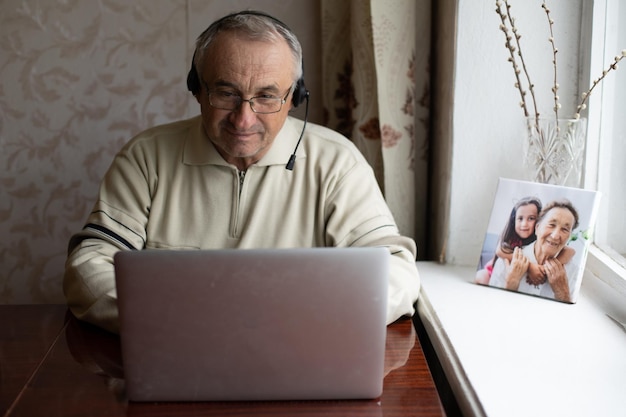 Elderly man with glasses using laptop at home.