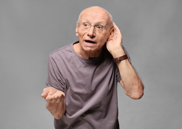 Elderly man with hearing problem on grey background