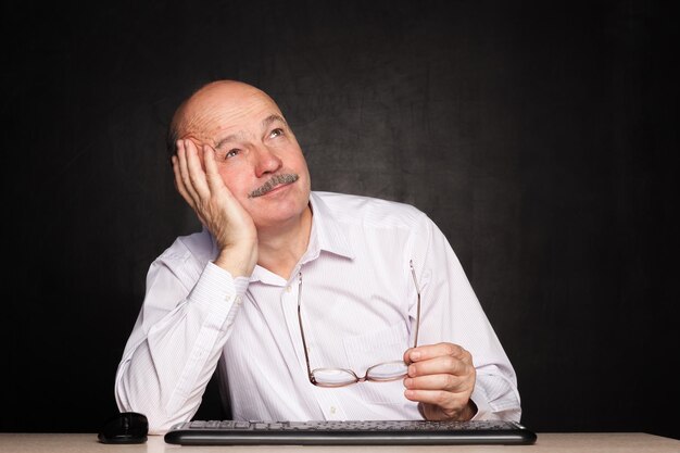 Elderly man at work dreamily looks away during a break thoughts on vacation salary increase or desire