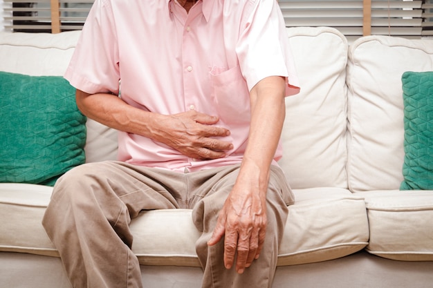 Elderly men have abdominal pain sitting on the sofa in the house