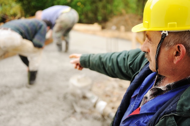 Elderly menager on workplace with workers on fresh concrete