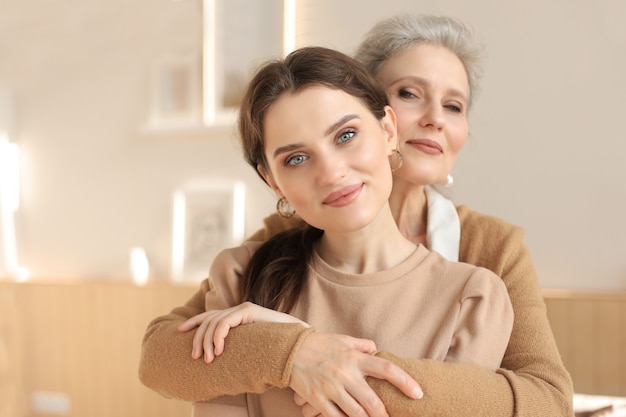 Elderly middle mother sitting in a chair and her daughter are hugging, looking at camera, trusted relations.