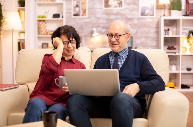 Пожилая пара с помощью современного ноутбука пообщаться со своим внуком. Бабушка и дедушка с использованием современных технологий