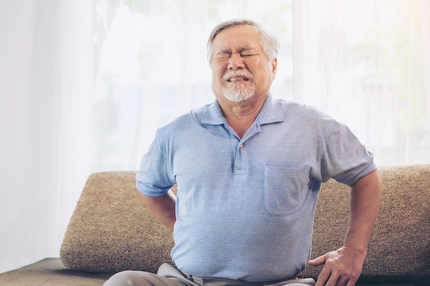 ソファの上の高齢患者、腰痛に苦しんでいるアジアの年配の男性-医療とヘルスケアの概念