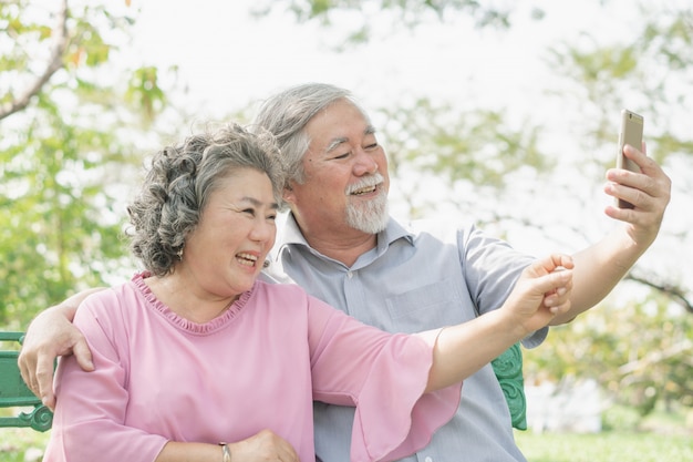 Elderly people lifestyles and communication technology. Happy grandparent using tablet video call and talking with family in the park.