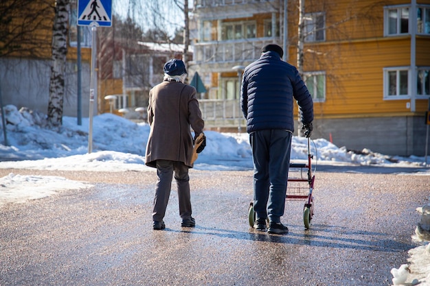 Пожилые люди идут с ходунками по заснеженной улице